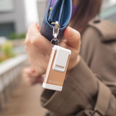 K6R Keychain Light a compact white and bronze LED torch attached to a keyring and held at a blue bag zipper