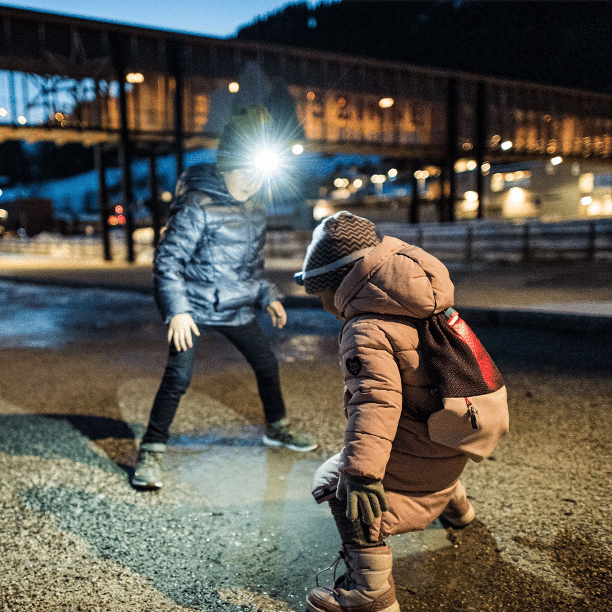 Kidled2 Headlamp worn by child in brown jacket with backpack outdoors at night while another person nearby wears a bright headlamp