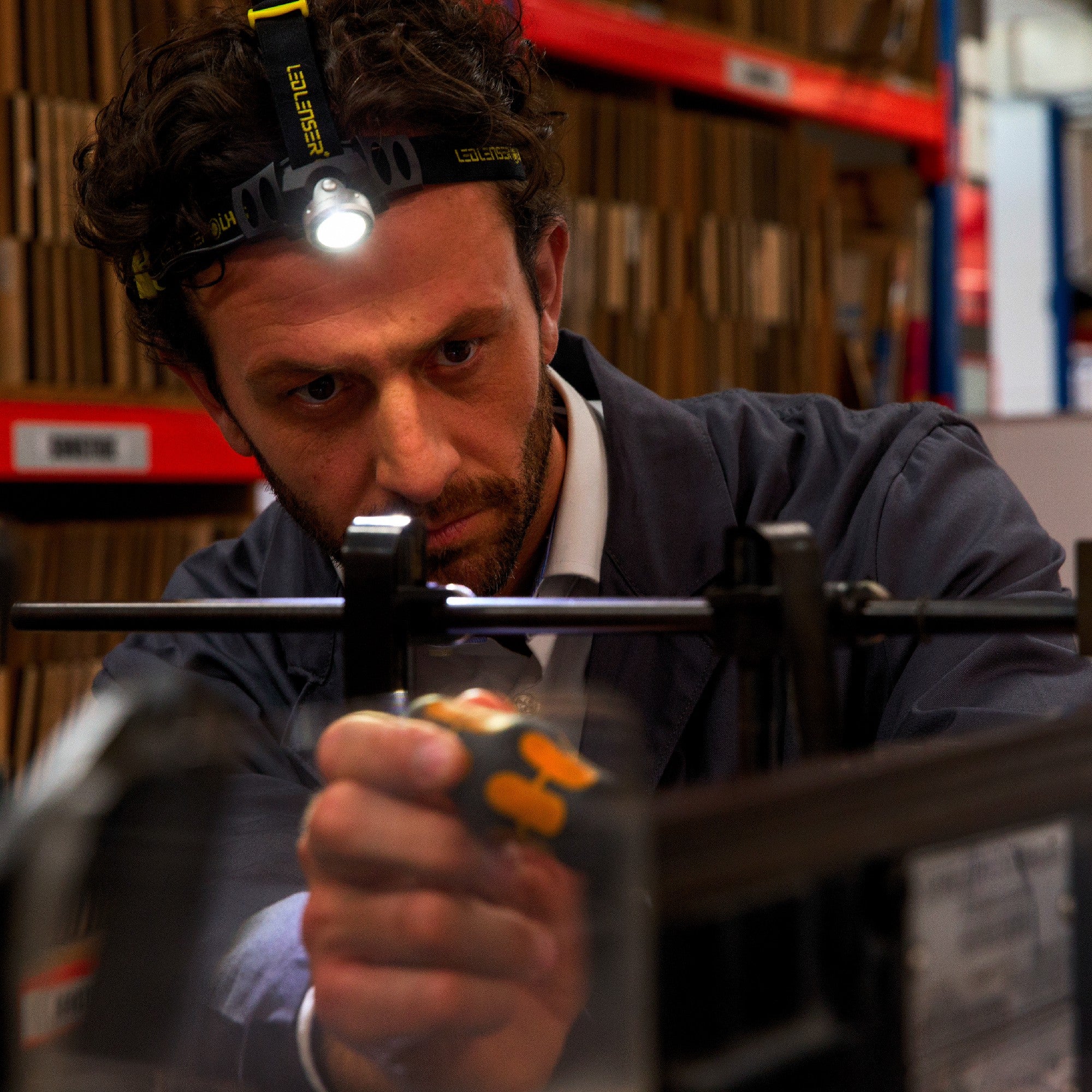 iH6R Rechargeable Headlamp worn by a man in a workshop with a headband light on inspecting a tool set