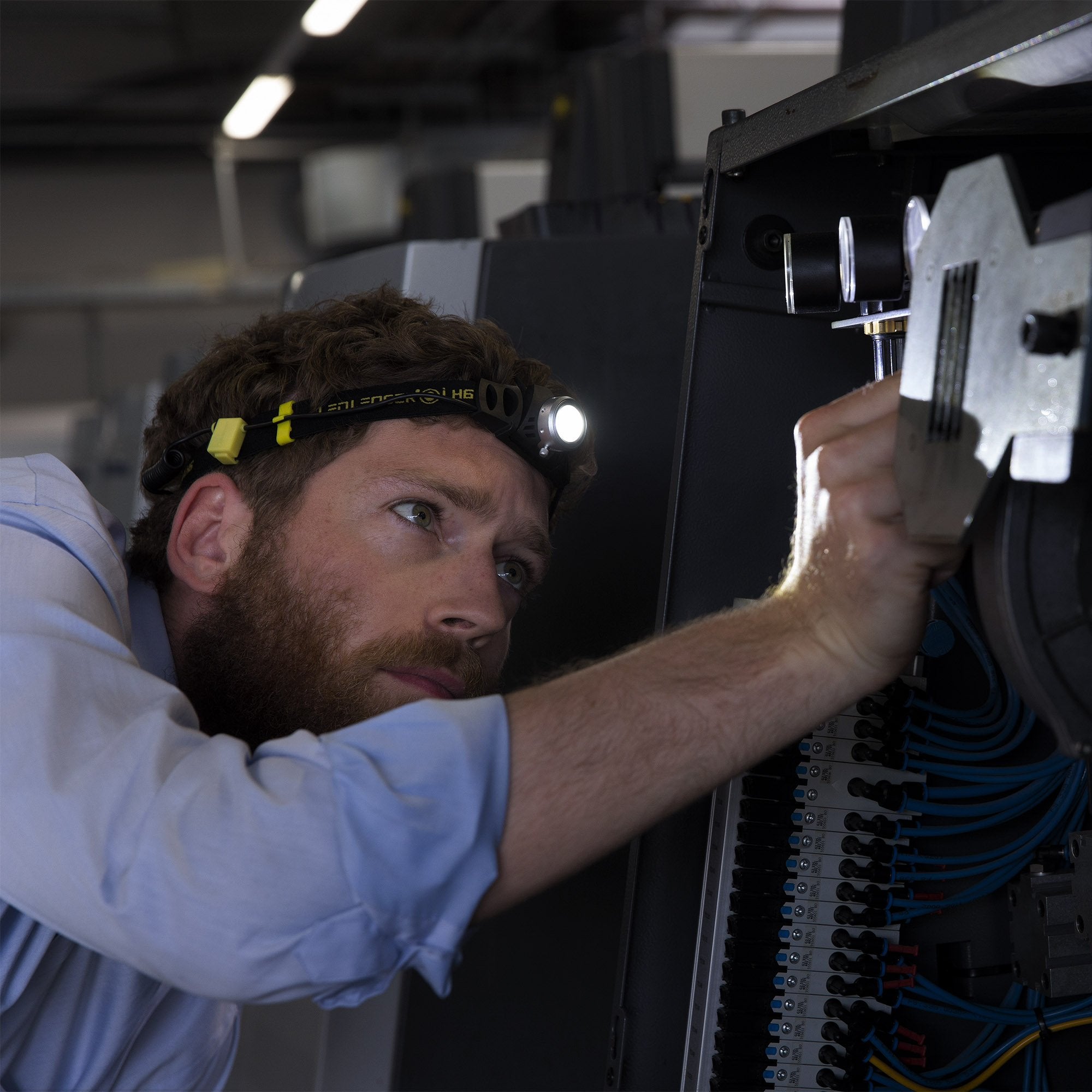 iH6R Rechargeable Headlamp worn by a technician inspecting an electrical panel with exposed wiring and components