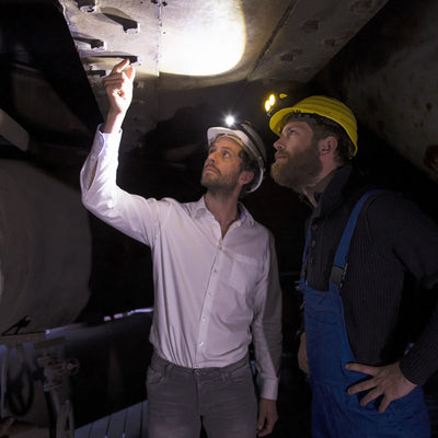 Ledlenser iSEO3 Headlamp shown on a white helmet as two professionals inspect a dark industrial site with headlamps illuminated
