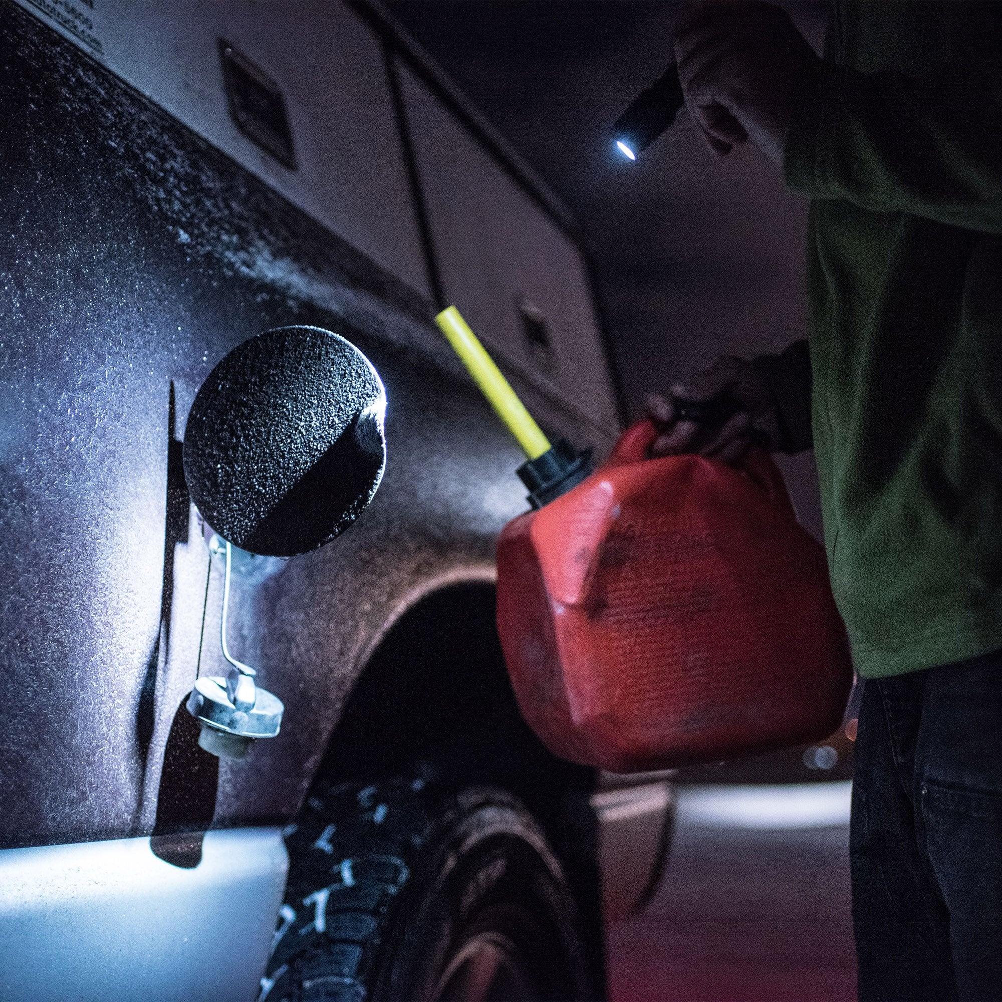 Ledlenser F1 Torch held by a person shining light on a red jerry can beside a car wheel in a dark workshop