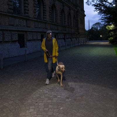 H7 2 Headlamp worn by a person in a yellow rain jacket walking a dog on a dimly lit cobblestone path at night