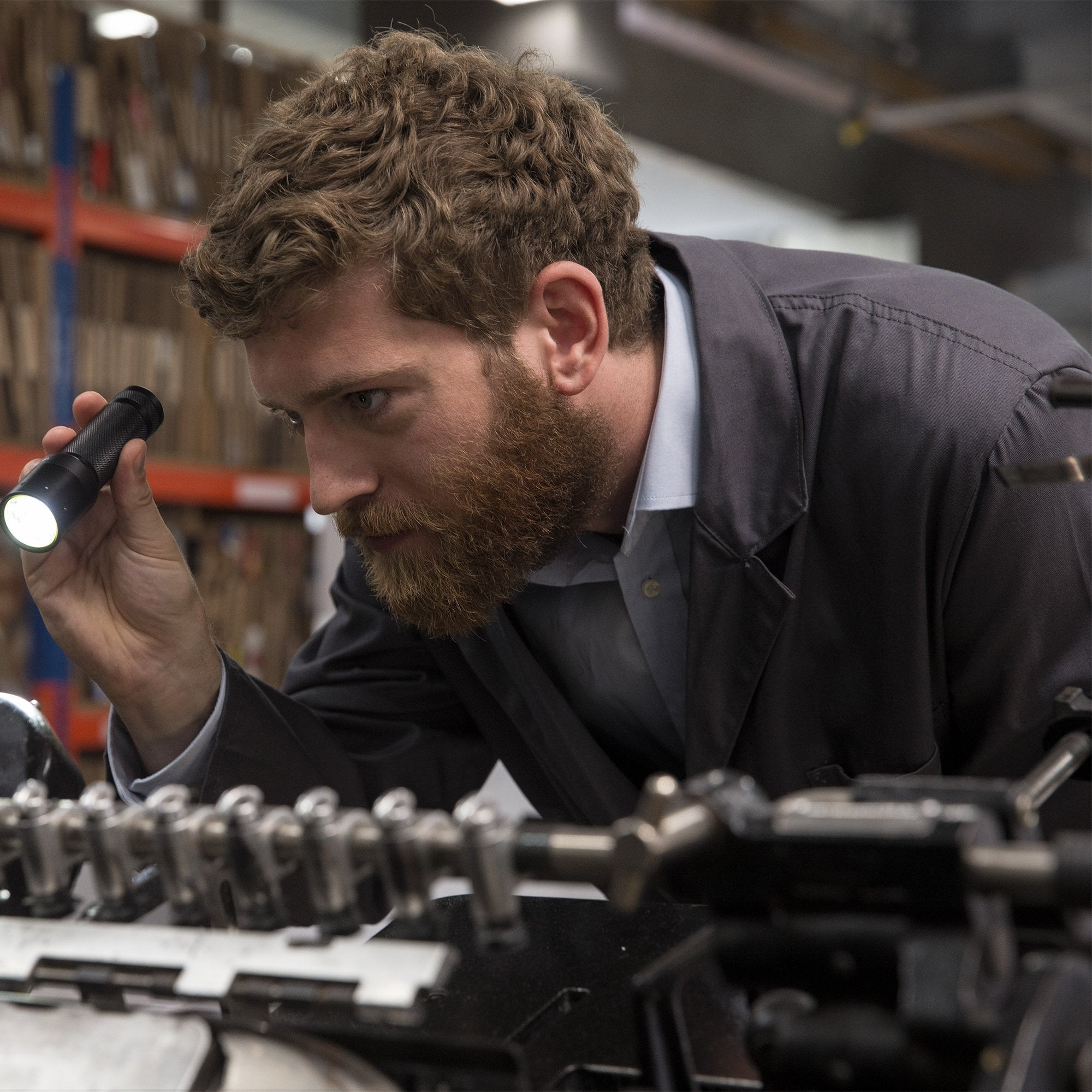 i9R Rechargeable Torch held by a man in a workshop inspecting industrial equipment with the flashlight beam