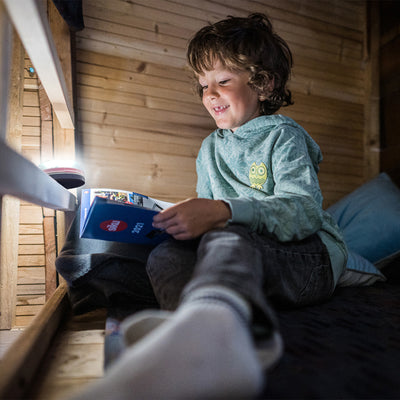 Ledlenser Kidcamp6 Lantern battery operated children's lantern on a shelf lighting a child reading inside a wooden shed