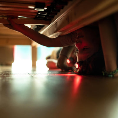 Kidled4R Headlamp worn by child crawling under a table red light emitted from the headlamp indoor setting