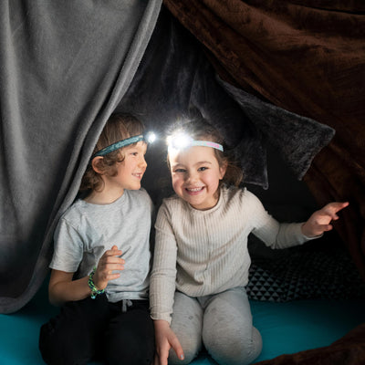 Kidled4R Headlamp worn by two children inside a dark tent one with bright light on wearing grey and cream clothing