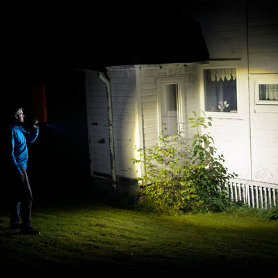 P17R Core Torch handheld light directed at a white house exterior at night person in a blue jacket holding the beam