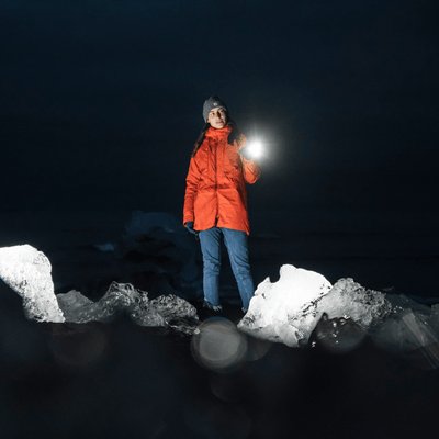 Ledlenser P18R Signature Torch held by a person in an orange jacket at night on rocky terrain