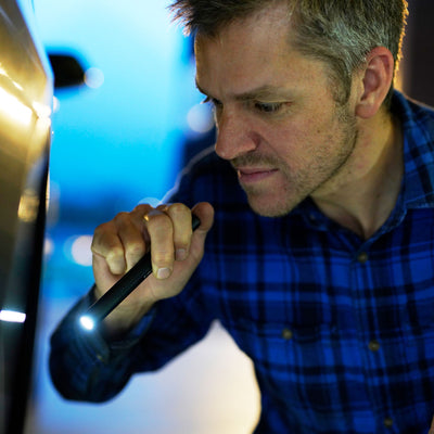 Ledlenser P4 Core Torch handheld by a man in a blue plaid shirt beam directed at a surface in a workshop setting