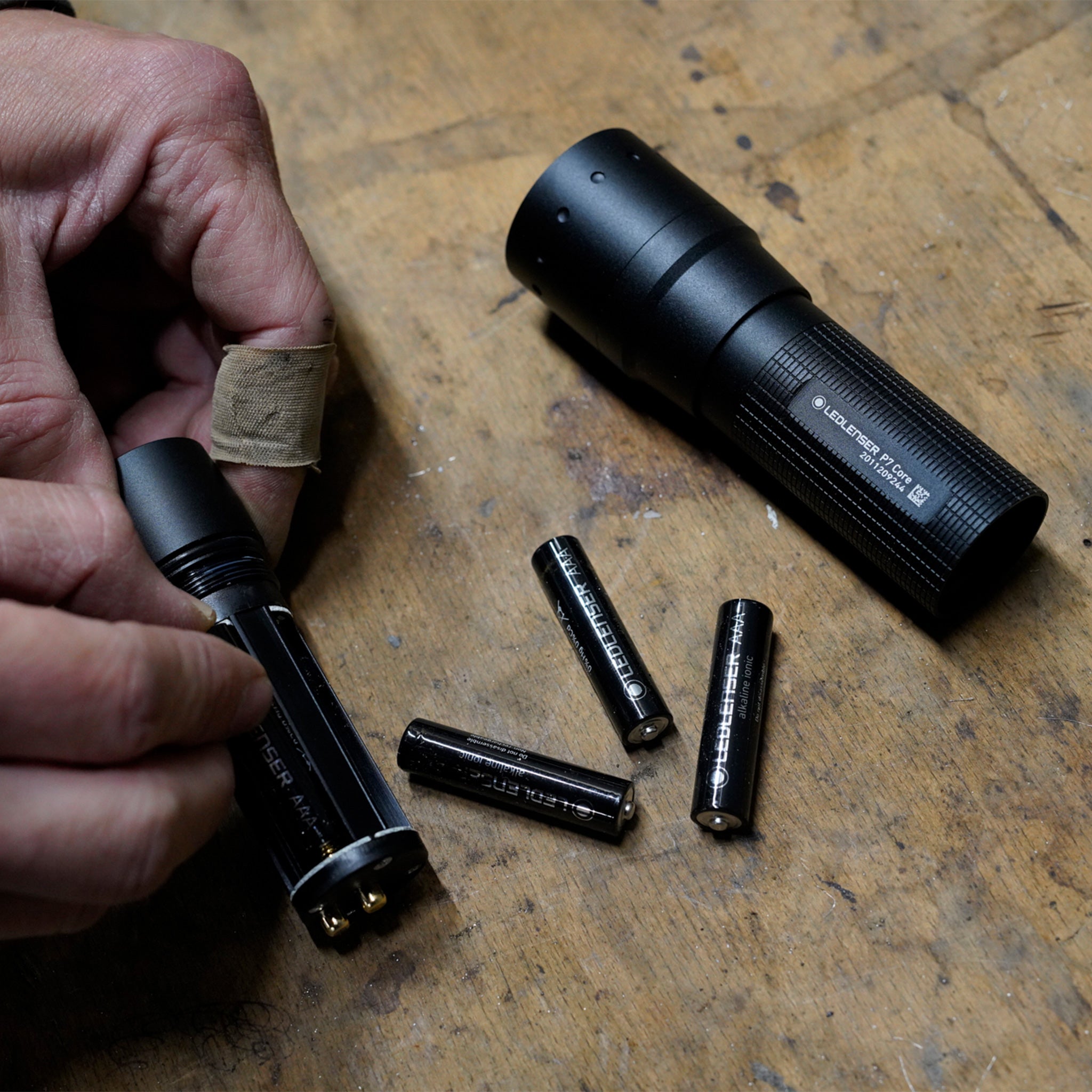 Ledlenser P7 Core Torch disassembled on a wooden workbench with batteries and the battery compartment being prepared by hand