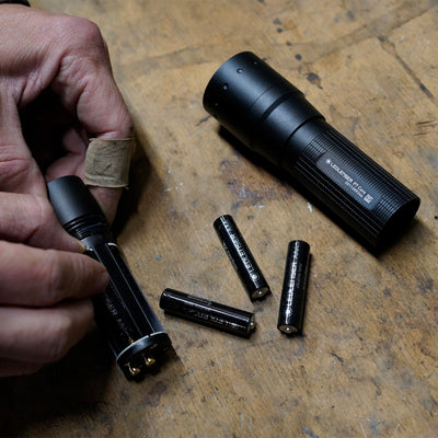 Ledlenser P7 Core Torch disassembled on a wooden workbench with batteries and the battery compartment being prepared by hand