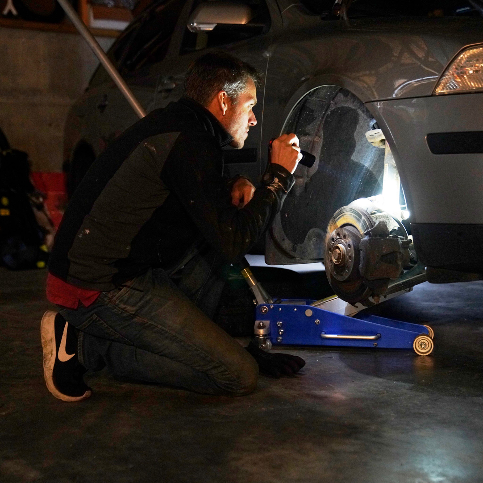 Ledlenser P7 Core Torch being used by a mechanic kneeling beside a car on a floor jack in a workshop