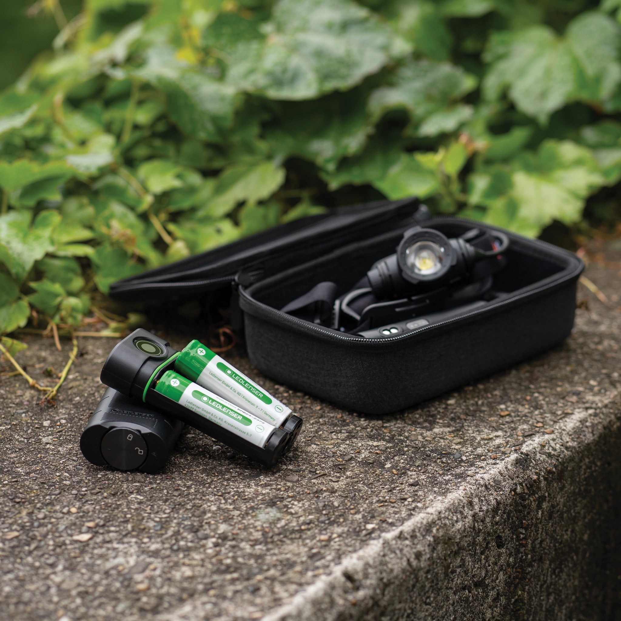 Flex7 Powerbank with two green Ledlenser rechargeable batteries and a black case housing a headlamp on a stone surface