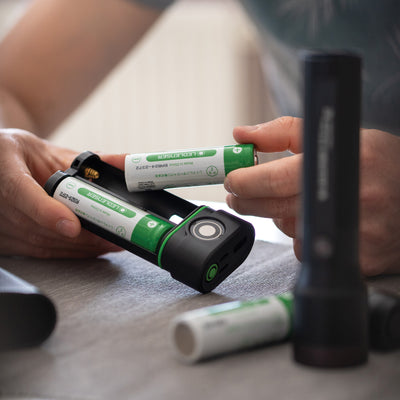 Flex10 Powerbank with two green battery cells being inserted into its black charging unit hands handling batteries on a table