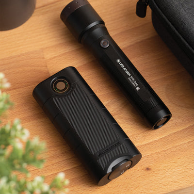 Flex10 Powerbank on a wooden surface beside a black cylindrical device with a circular status indicator near a button