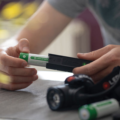 Flex5 Powerbank in use as a green Ledlenser battery is inserted into its black charging unit shown with hands on a table