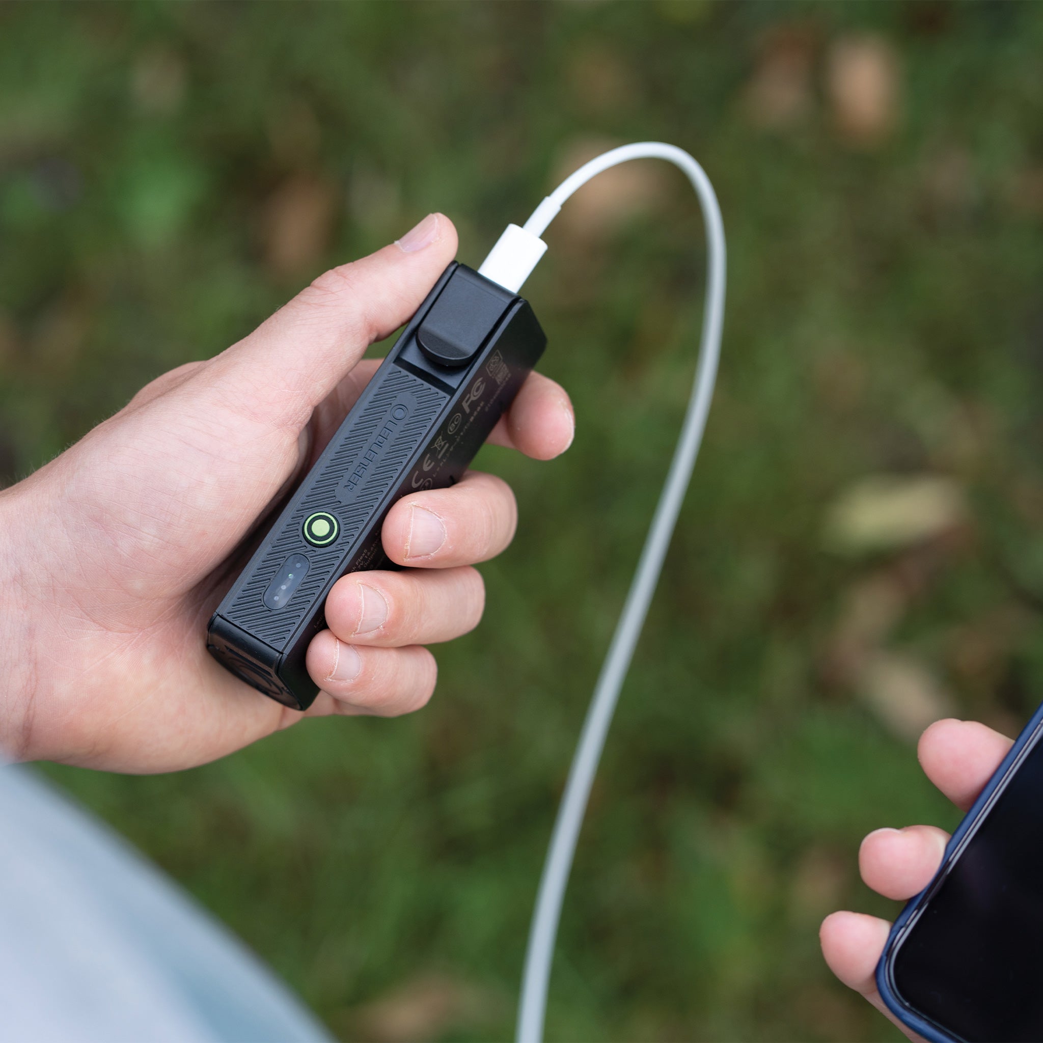 Ledlenser Flex5 Powerbank held in left hand with a white USB‑C cable connected to a smartphone outdoors