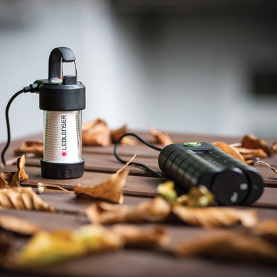 Ledlenser Flex7 Powerbank standing upright beside a black Ledlenser portable light on a wooden table with autumn leaves