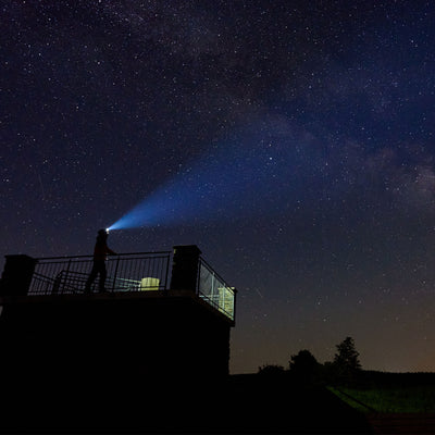 MH10 Headlamp being used by a person on a balcony at night blue beam projected into a starry sky