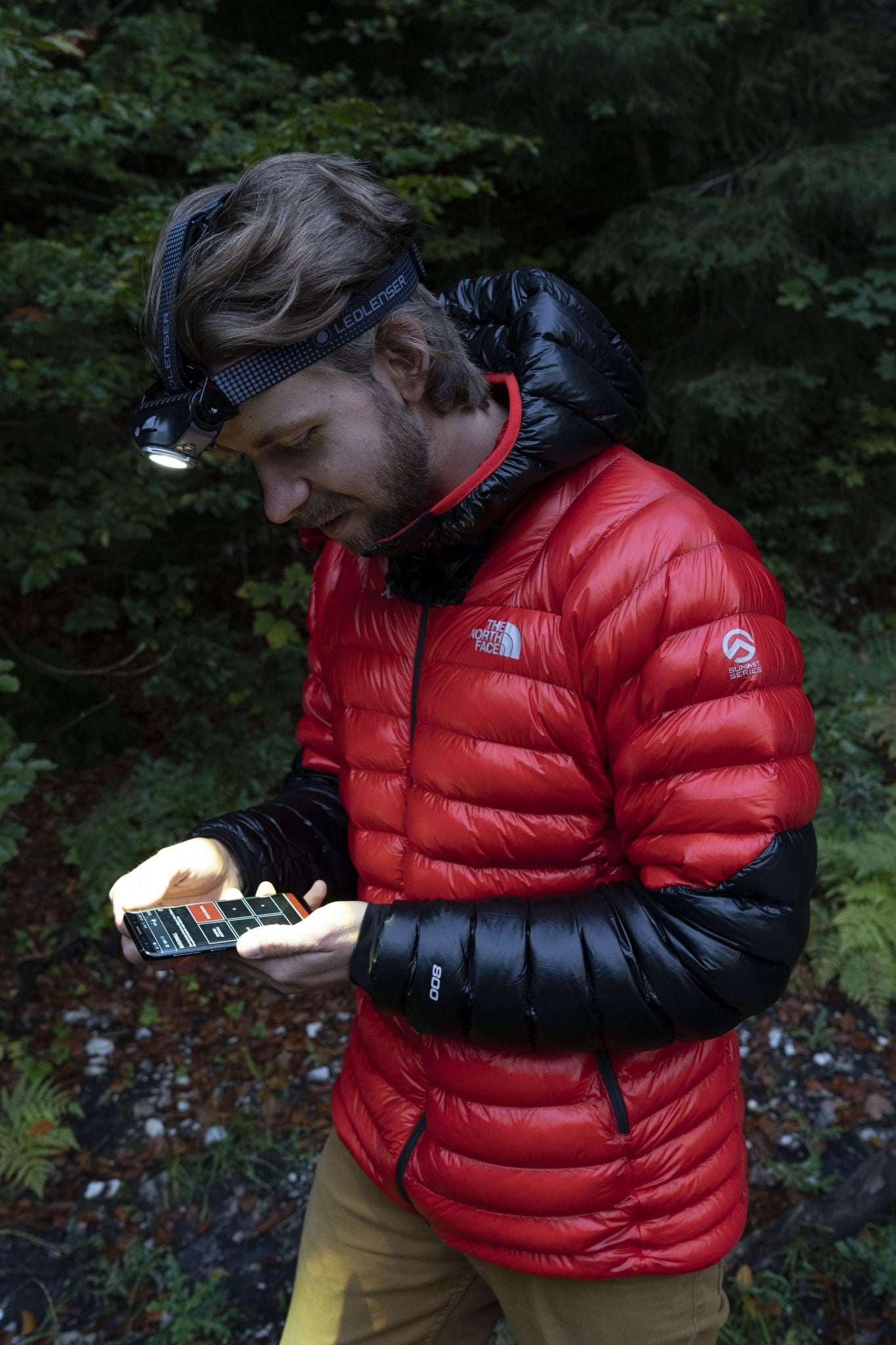 MH11 Blue Outdoor Headlamp worn on the head by a man in a red jacket outdoors with the headlamp illuminated