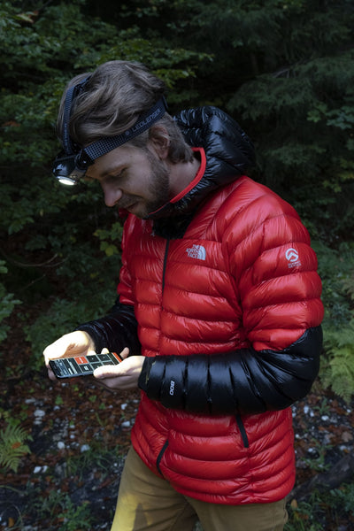 MH11 Blue Outdoor Headlamp worn on the head by a man in a red jacket outdoors with the headlamp illuminated