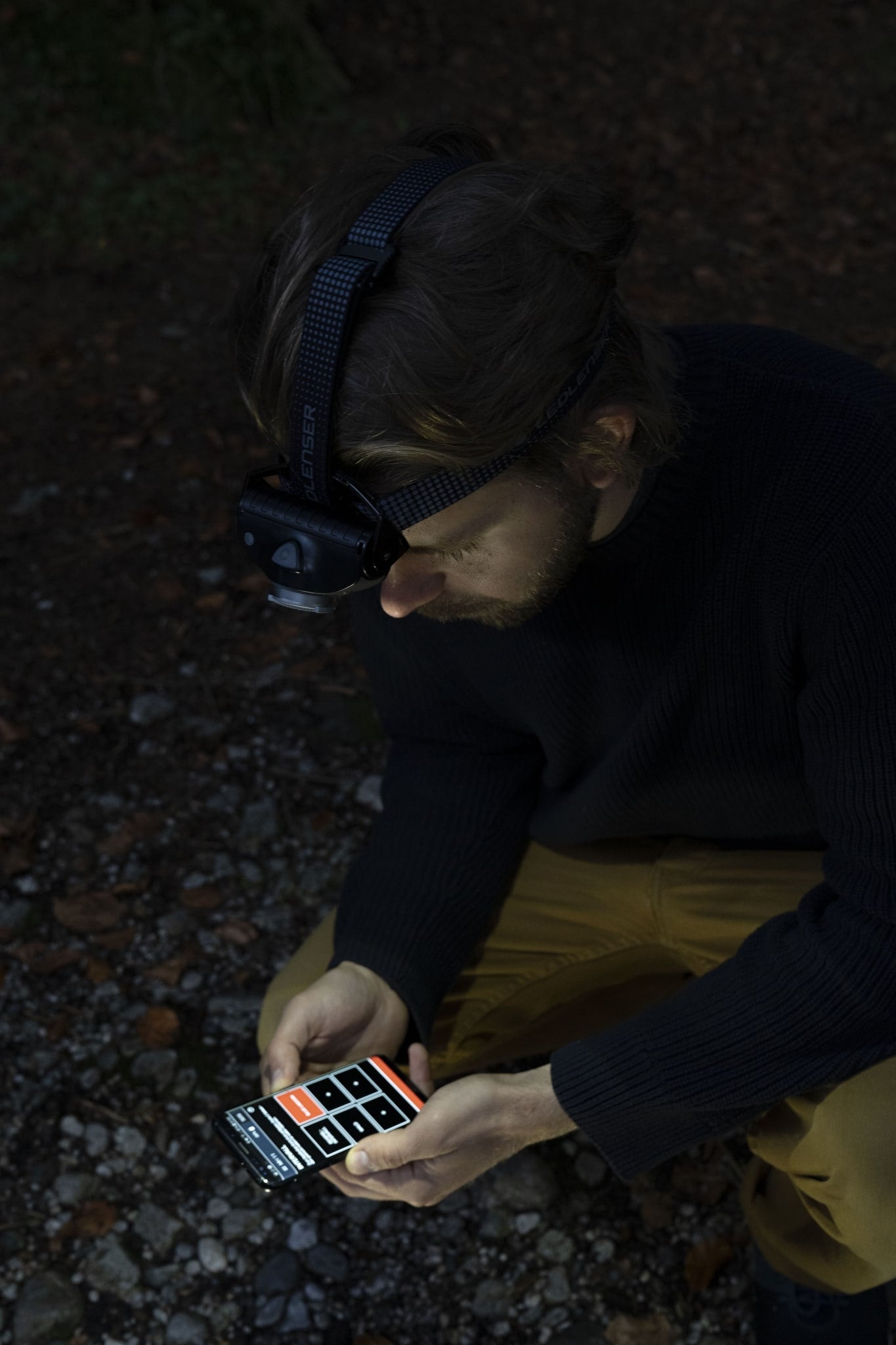 Ledlenser MH11 Blue Outdoor Headlamp worn on a head with a blue strap outdoors man looking at a smartphone