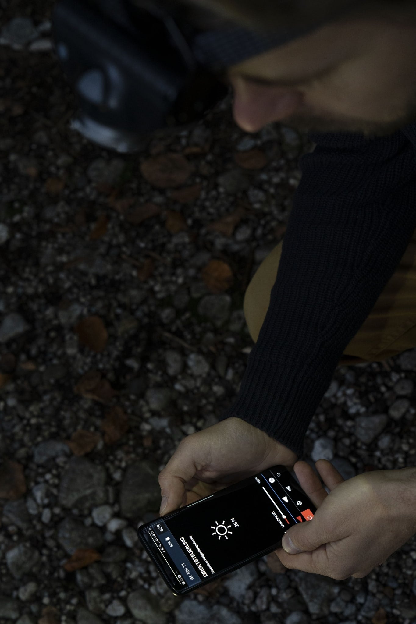 MH11 Blue Outdoor Headlamp displayed on a smartphone screen held by a person outdoors with a rocky ground background