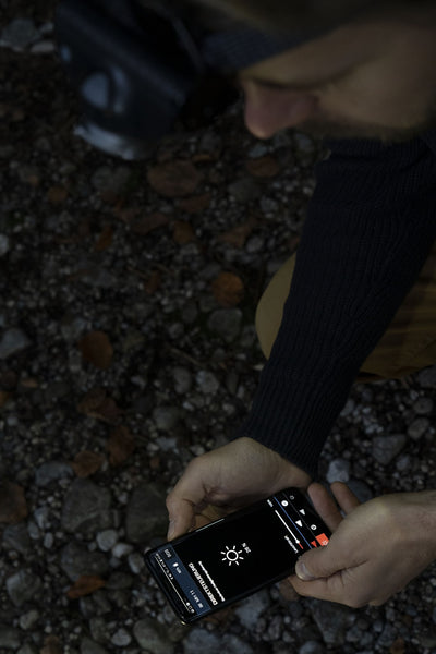 MH11 Blue Outdoor Headlamp displayed on a smartphone screen held by a person outdoors with a rocky ground background