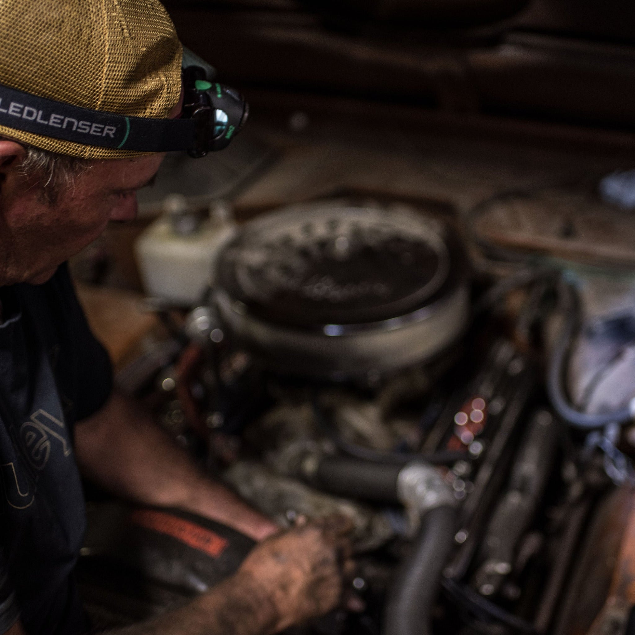 MH2 Headlamp worn by a technician in a dusty engine bay with a Ledlenser headlamp strap and visible engine components