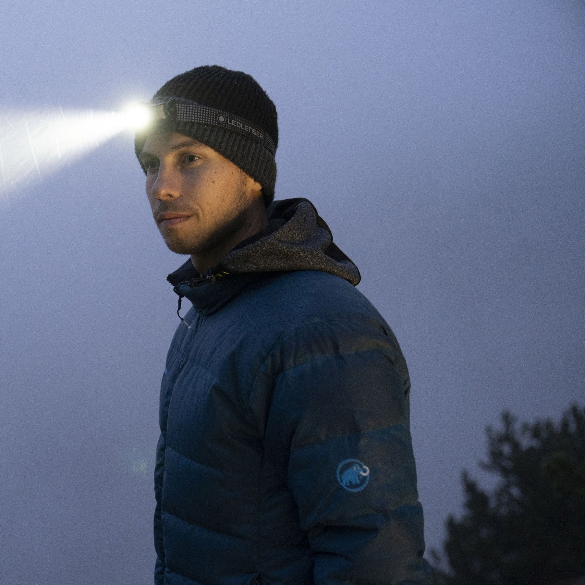 Ledlenser MH5 Outdoor Headlamp worn on a beanie by a man bright beam projecting forward in low light
