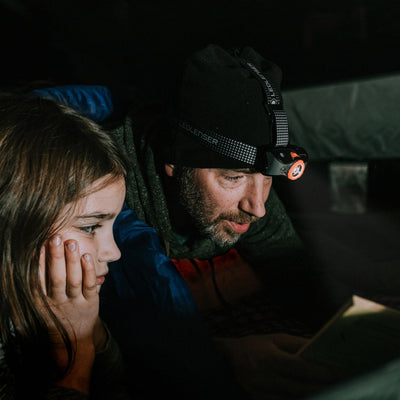MH7 Outdoor Headlamp worn on a man's head with an orange accent ring in a dark tent branding on the strap