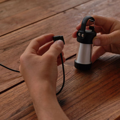 ML4 Lantern being held by hands compact rechargeable Ledlenser area light with black top handle and silver ribbed body on a wooden surface