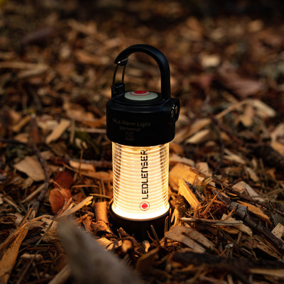 Ledlenser ML4 Warm Light Lantern shown upright on a forest floor black top housing with red button ribbed glowing body