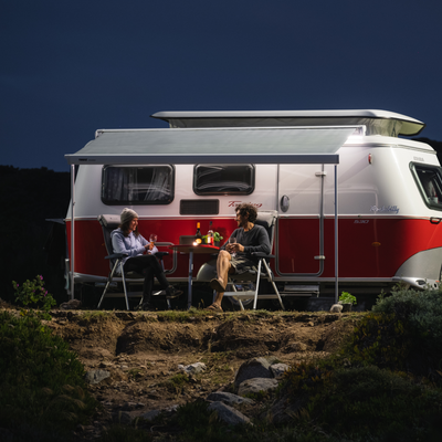 Ledlenser ML4 Lantern placed on a table beside two campers seated near a white and red caravan under an awning at night