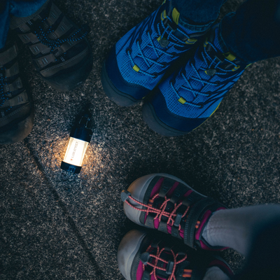 ML4 Lantern on rocky ground between blue hiking shoes and a gray shoe lantern lit