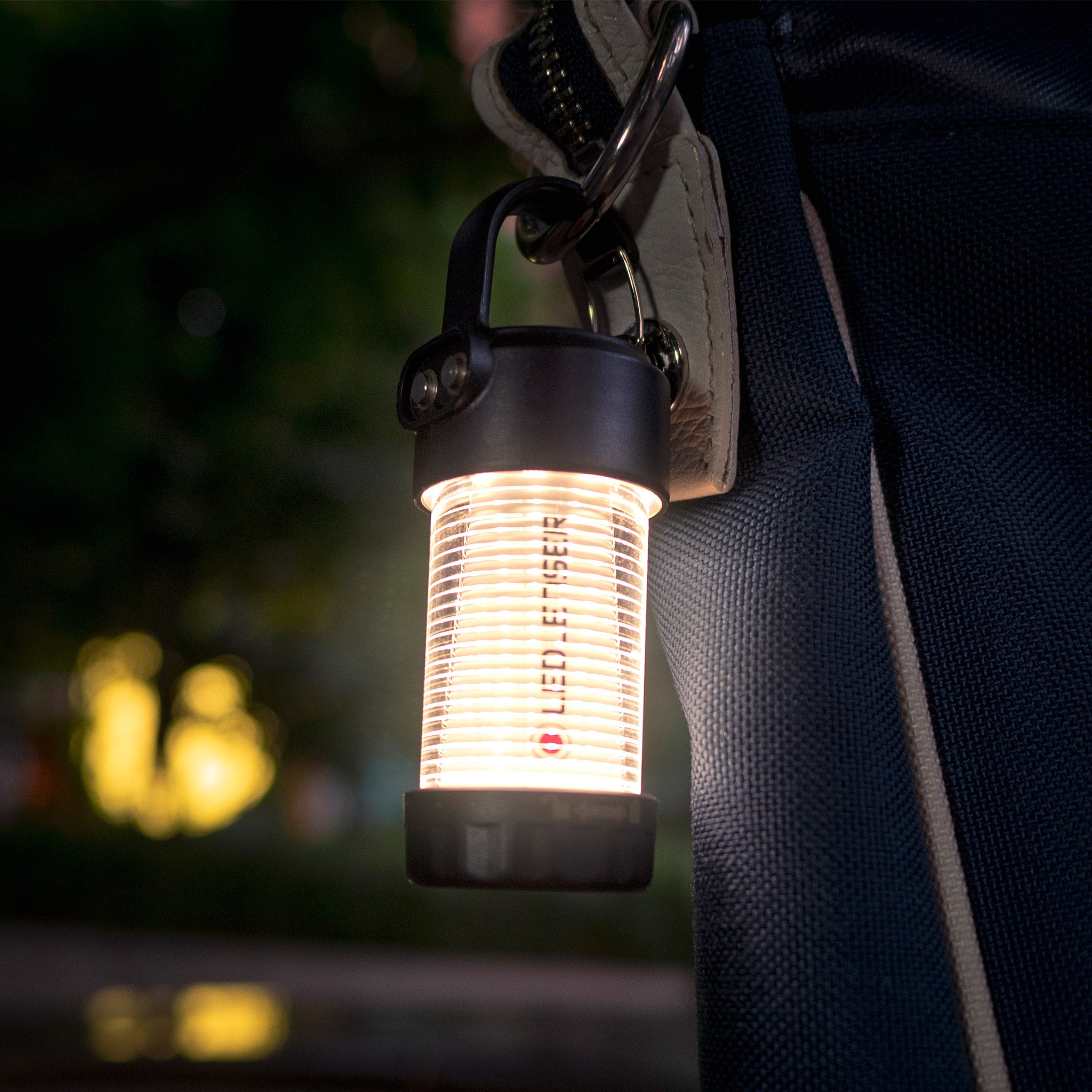ML4 Warm Light Lantern hanging from a strap with a carabiner glowing warm light; compact ribbed lantern by Ledlenser