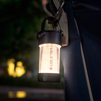 ML4 Warm Light Lantern hanging from a strap with a carabiner glowing warm light; compact ribbed lantern by Ledlenser