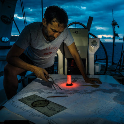 Ledlenser ML6 Lantern on a boat table emitting a red glow while a man examines a map with tools nearby