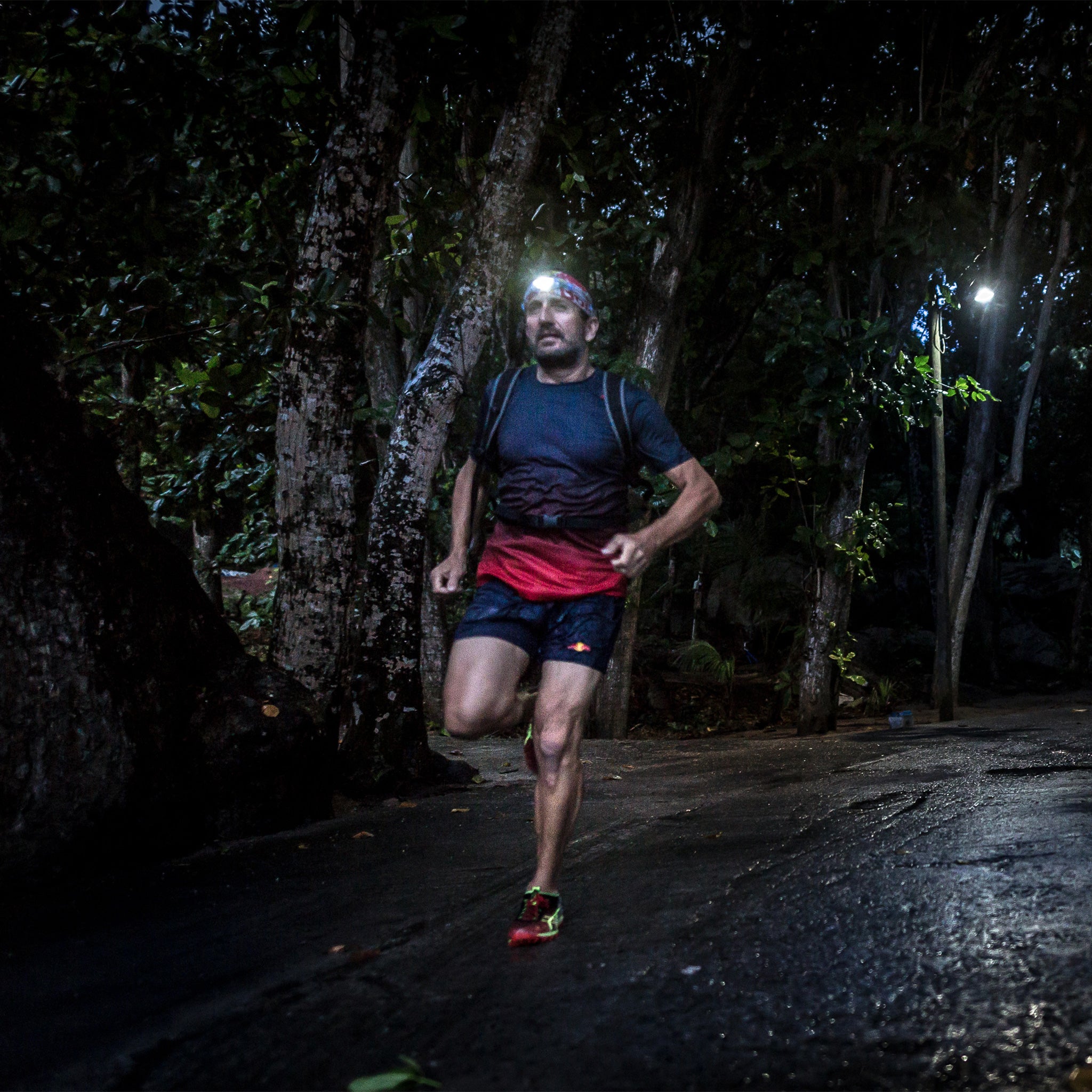 NEO4 Battery Operated Headlamp worn by a man running at night on a damp forest path with trees; headlamp lit