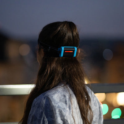 NEO3 Running Headlamp worn on a person's head with blue housing and black strap night city lights in background