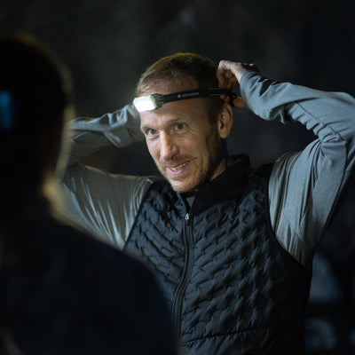 NEO5R Running Headlamp worn by man with the headlamp on in a dark setting Ledlenser branded headband and illuminated front light