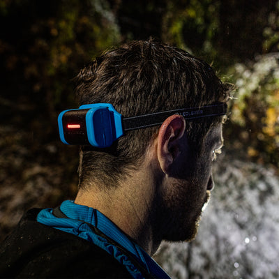 NEO9R Running Headlamp worn on a head strap by a person outdoors at night blue housing with a red indicator