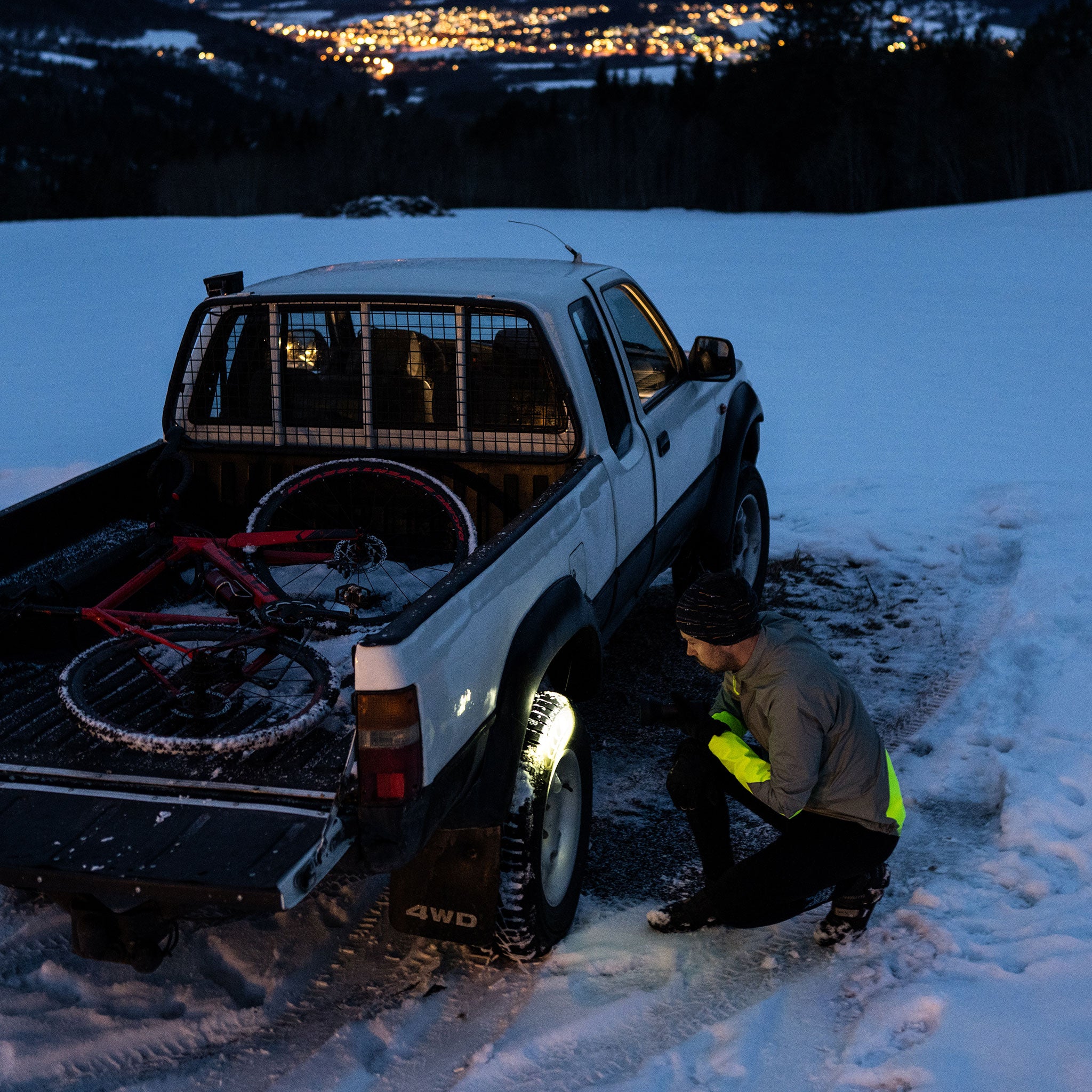 P18R Work Torch in use beside a white pickup on snowy terrain with a bike in the truck bed and a person in high‑visibility kneeling by the wheel