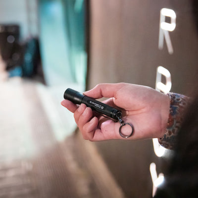 Ledlenser P3 Battery Operated Torch held in a hand compact black pocket flashlight with a keyring shown in a dim interior