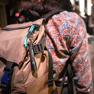P3 Battery Operated Torch attached to a turquoise cord on a tan backpack worn by a person in a patterned shirt