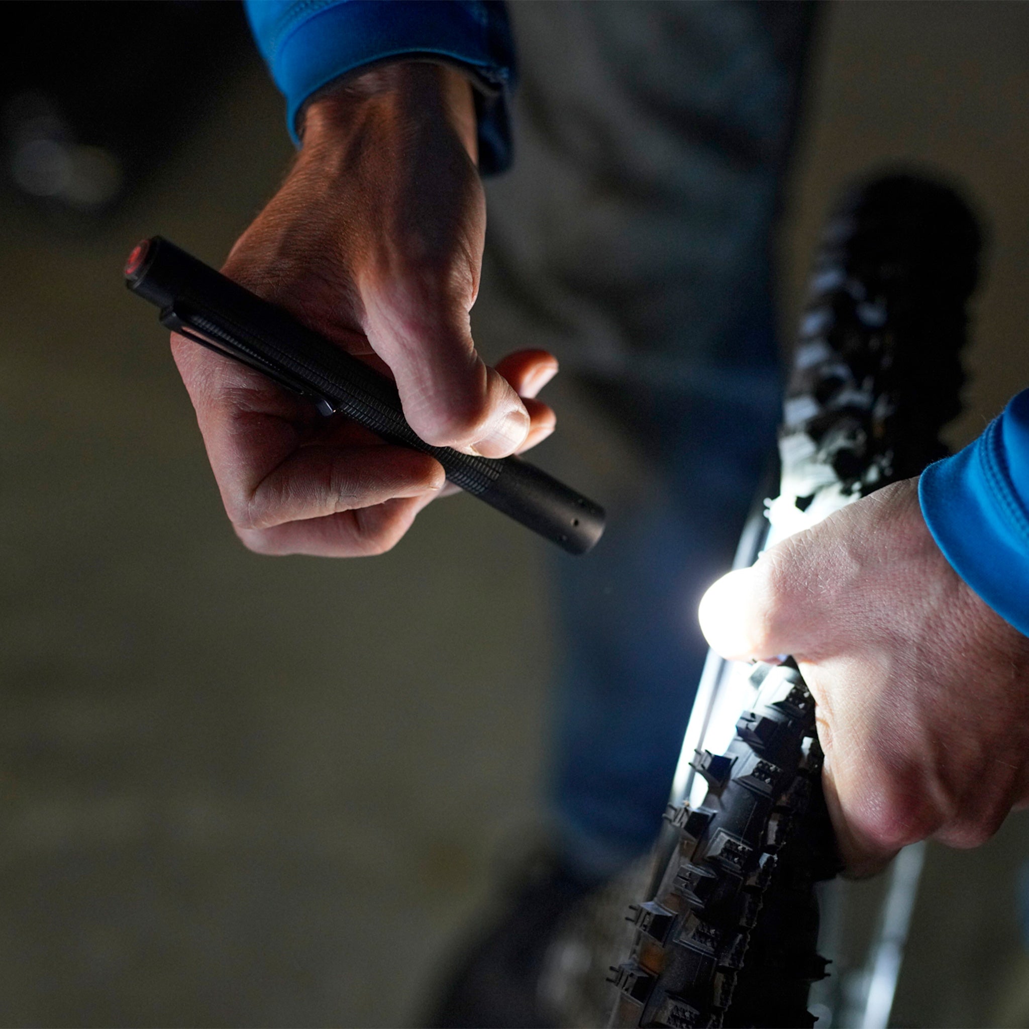 P4 Core Torch held in a hand beside a bicycle tire close up black pen‑style LED torch