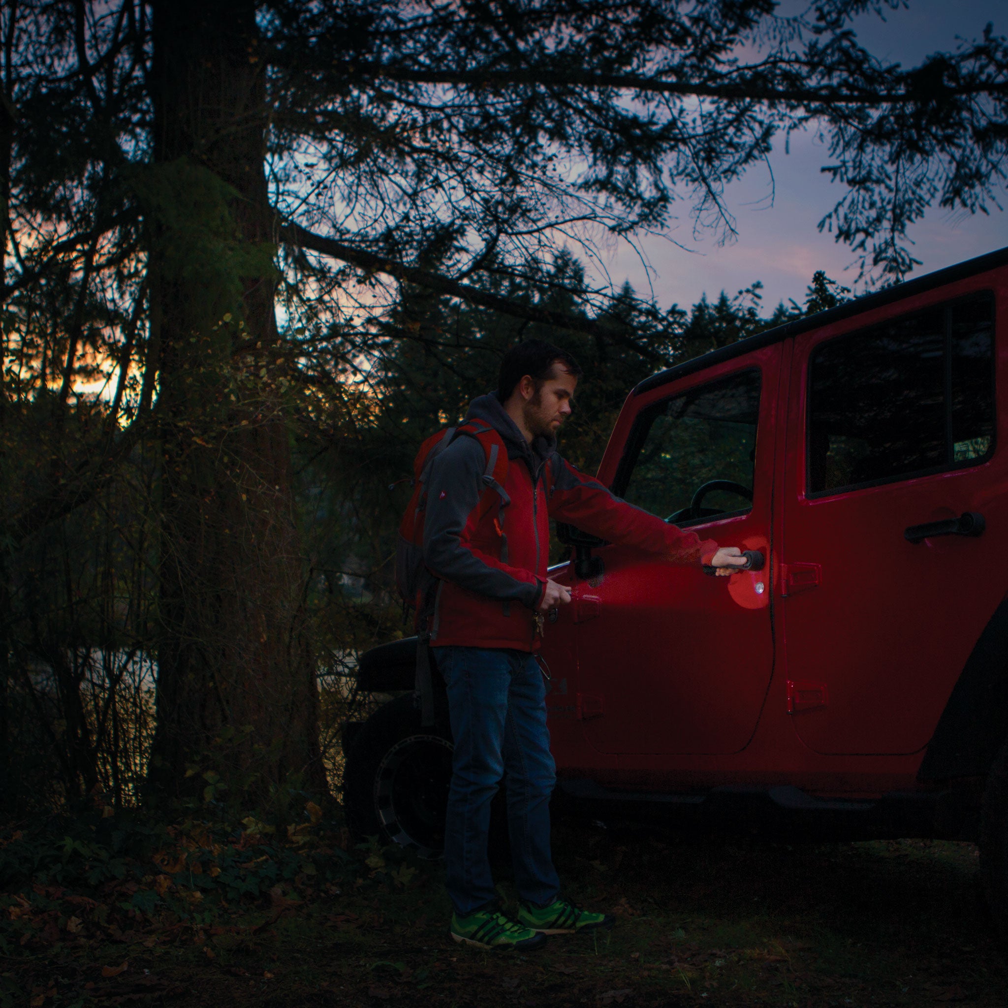 Ledlenser P4 Torch held by a man outdoors beside a red SUV at dusk with trees in the background