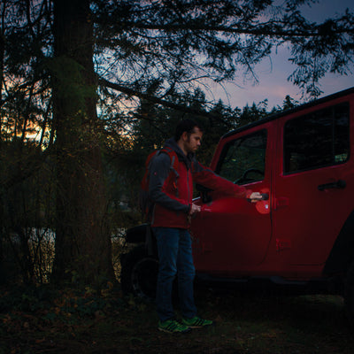 Ledlenser P4 Torch held by a man outdoors beside a red SUV at dusk with trees in the background