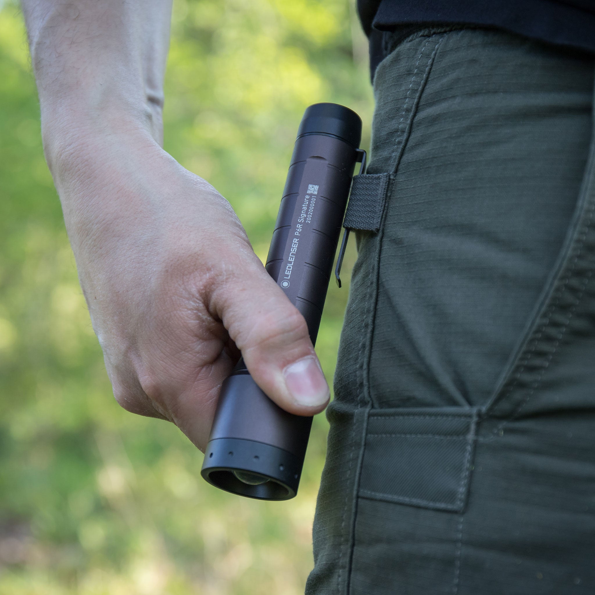 Ledlenser P6R Signature Torch held vertically by a person wearing green cargo pants with the clip visible on the side